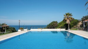 Una piscina azul cristalina con vistas al mar, rodeada de follaje y una valla.