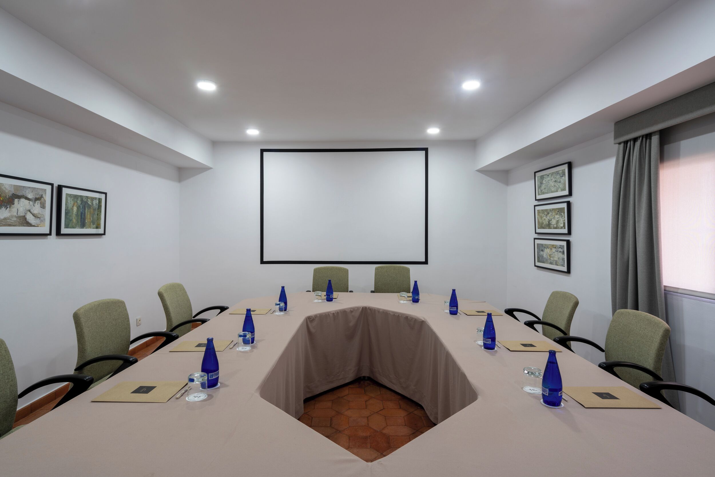 Un salón de conferencias con una larga mesa, sillas y una pantalla de proyector.