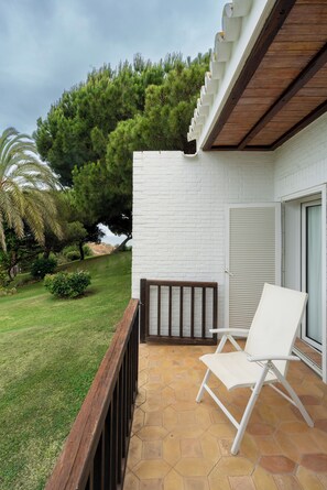 A patio with a white chair, a wooden railing, and a white brick wall. - Parador De Mazagon (Moguer)