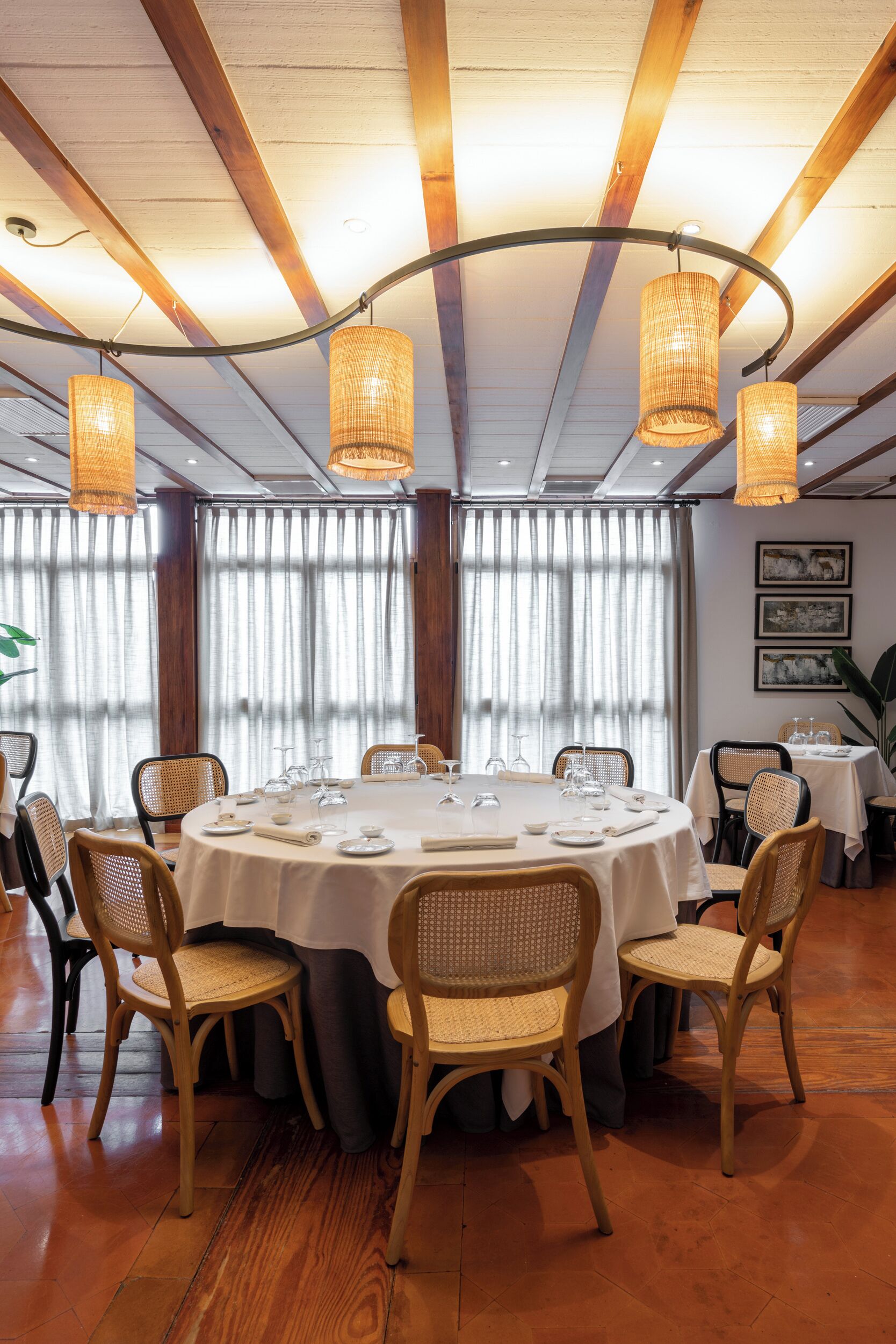 A dining area with round tables, wicker chairs, and hanging wicker lamps.