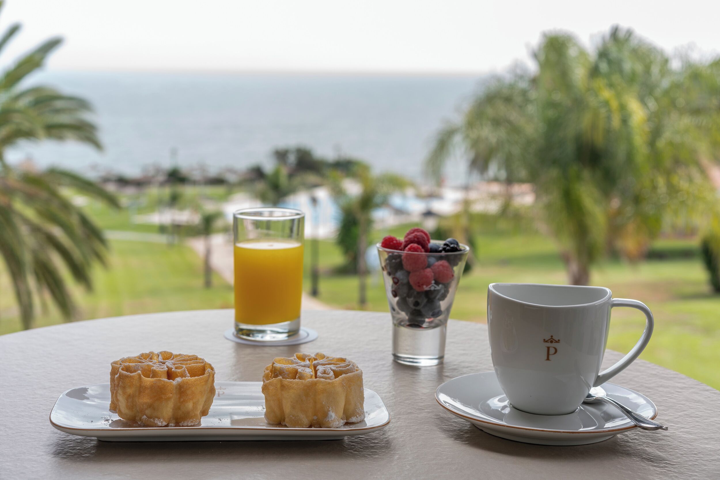 A breakfast setting with waffles, a glass of orange juice, and a cup of coffee on a table with a view of the ocean.