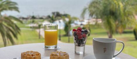 A breakfast setting with waffles, a glass of orange juice, and a cup of coffee on a table with a view of the ocean.