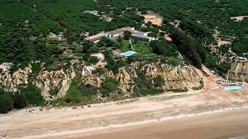 Vue aérienne d’une station balnéaire dotée d’une vaste plage, de zones boisées denses et d’un ensemble de bâtiments imposant.