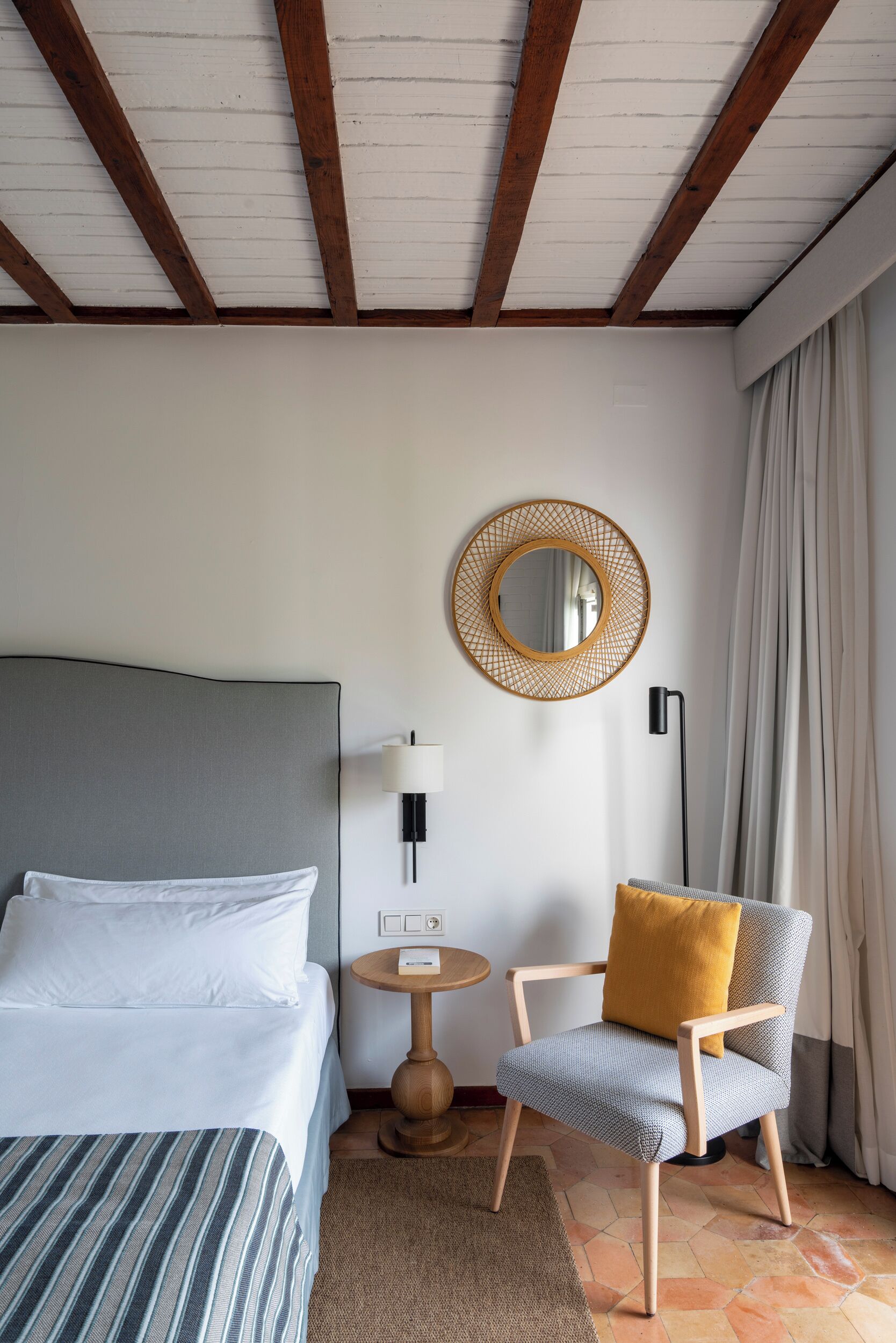 Ein Hotelzimmer mit einem Bett, einem Sessel, einem runden Spiegel, einer Lampe und einem kleinen Tisch.