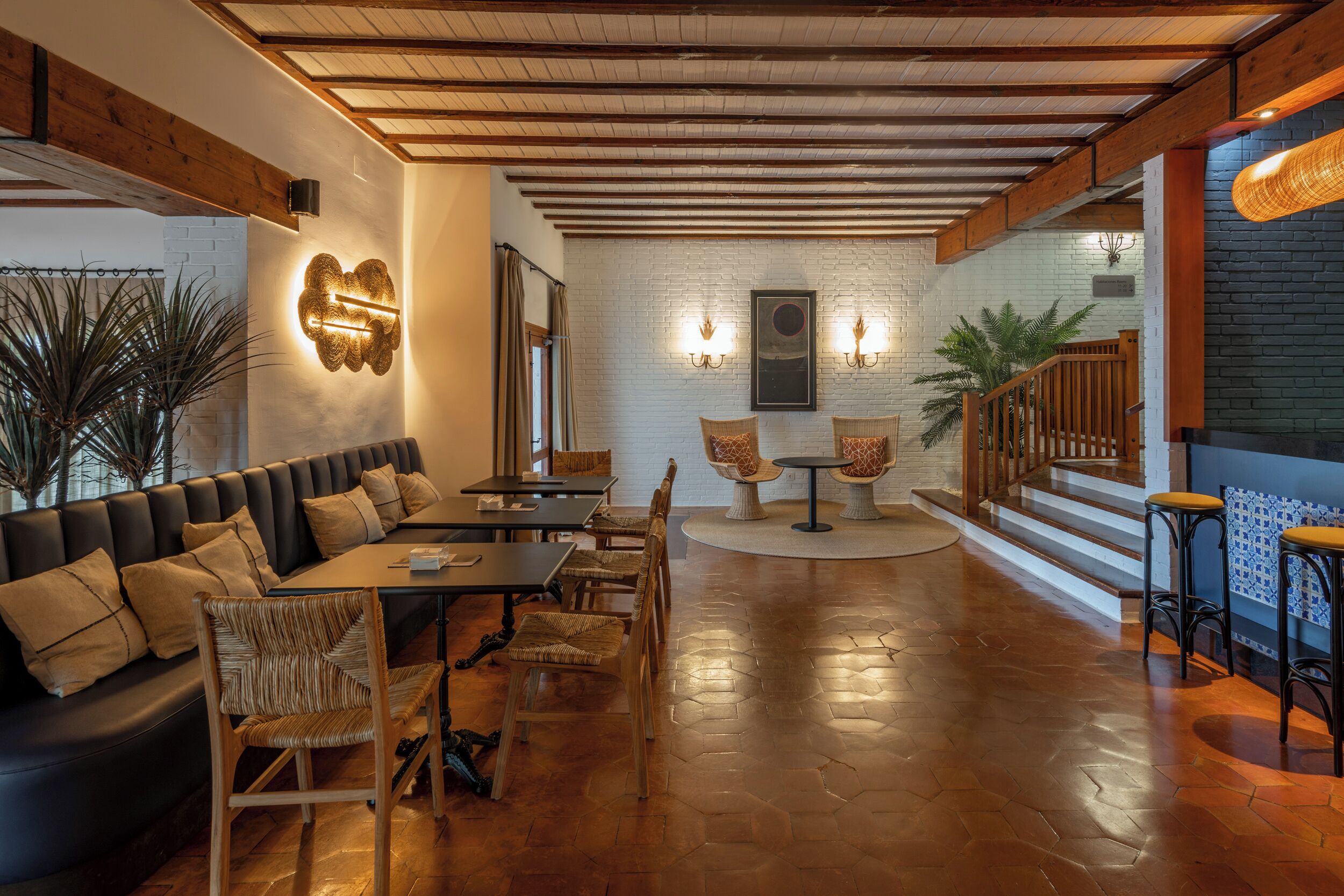 Un interior acogedor con techo de madera, un sofá de cuero negro, sillas de madera, una mesa redonda y una escalera con barandillas de madera.
