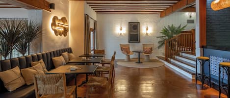 Un interior acogedor con techo de madera, un sofá de cuero negro, sillas de madera, una mesa redonda y una escalera con barandillas de madera.