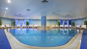 An indoor swimming pool with clear water, surrounded by lounge chairs and potted plants. - Palan Hotel (Erzurum)