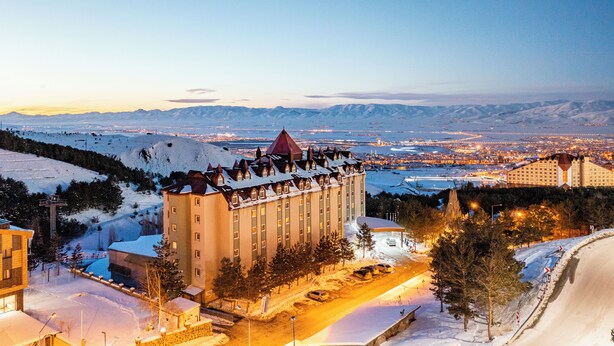 A hotel with a prominent red roof, situated in a snowy landscape with mountains in the background. - Palan Hotel (Erzurum)