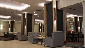 A modern lobby with grey armchairs, a wooden coffee table, and a dining area with a table and chairs. - Palan Hotel (Erzurum)