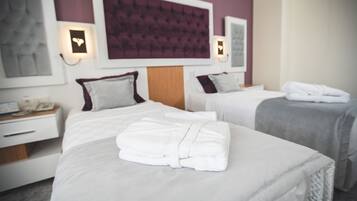 Habitación de hotel con dos camas, cada una con una almohada y una toalla doblada. Hay una mesita de noche con una lámpara y un teléfono.