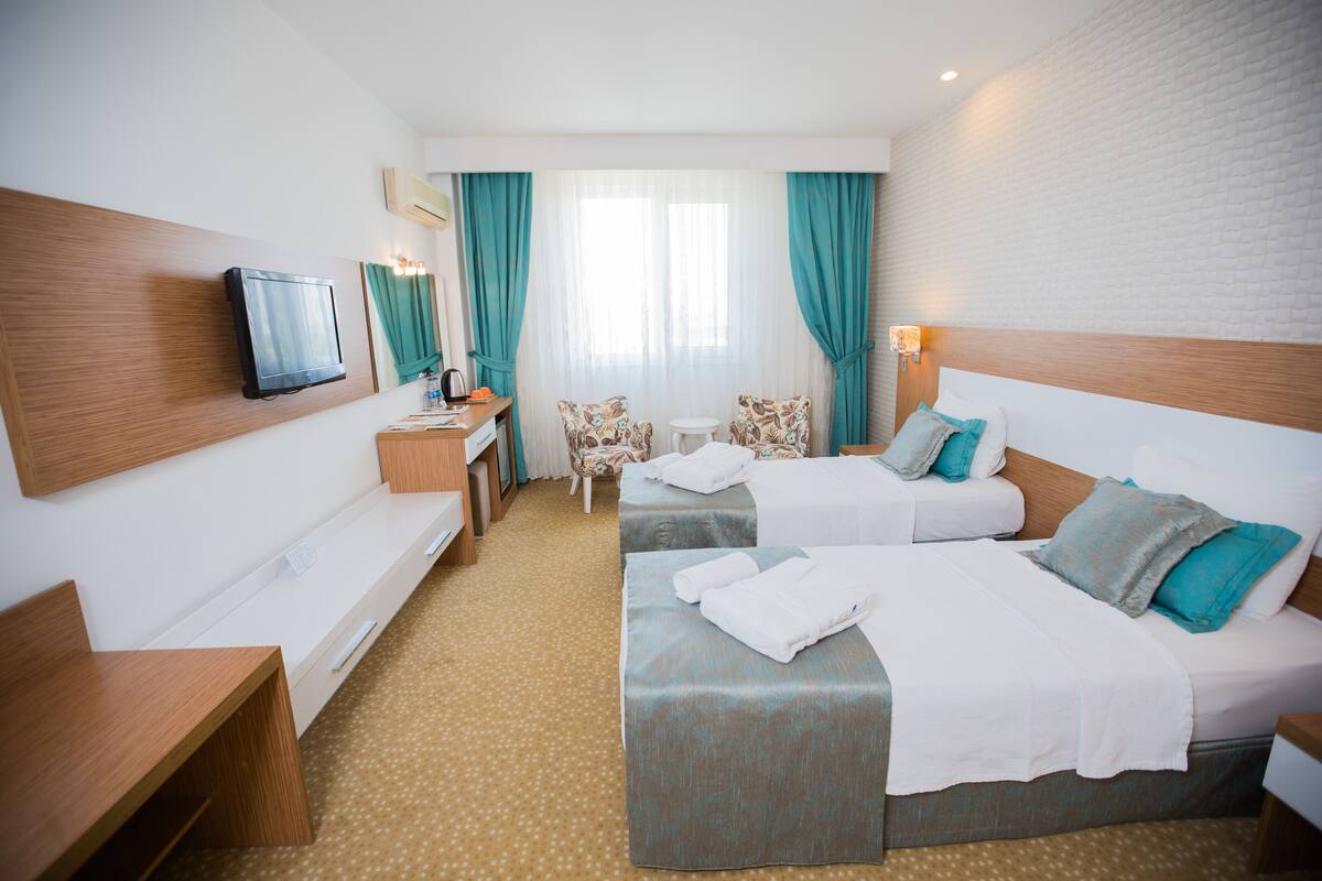Habitación de hotel con dos camas, un escritorio con silla, un televisor y una ventana con cortinas.