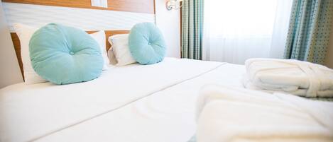 Una cama bien hecha con dos almohadas, cabecera y lámpara de pared.