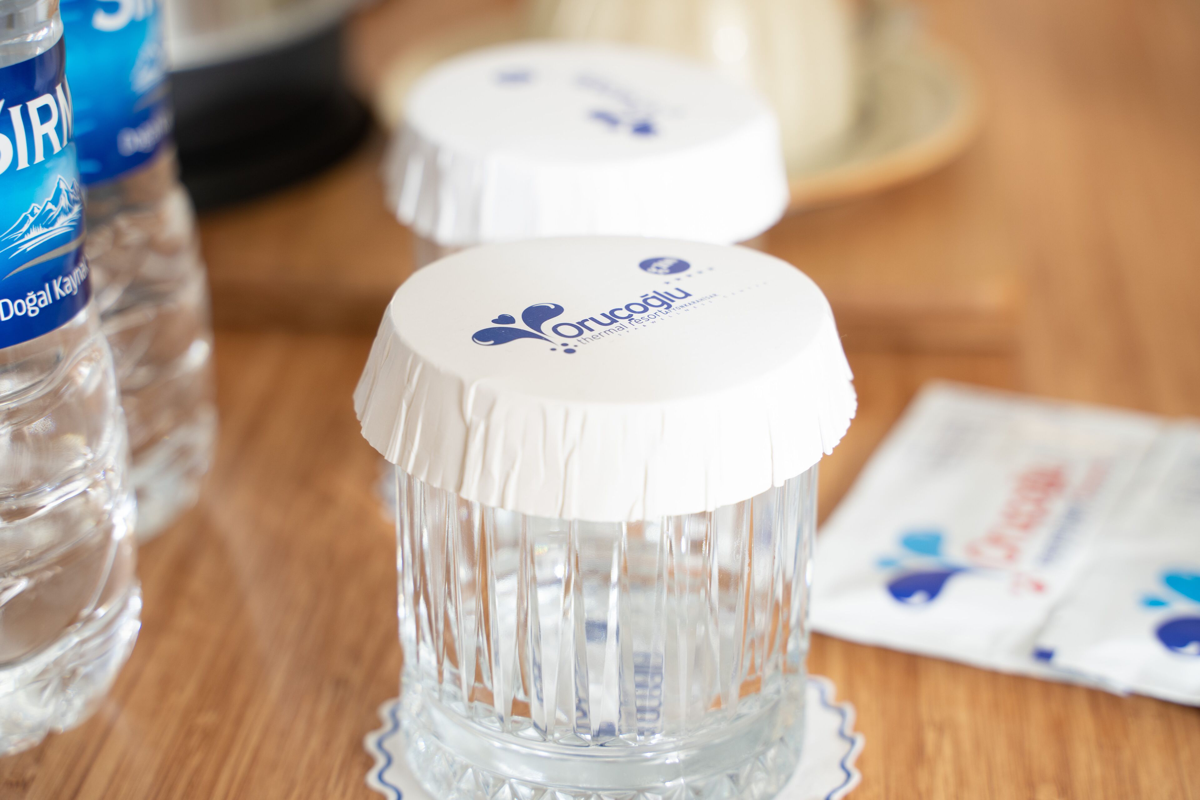 Una mesa con botellas de vidrio transparente y recipientes blancos con etiquetas azules.
