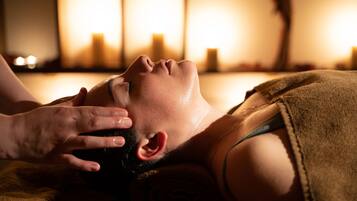 A person receiving a massage in a dimly lit room with candles.