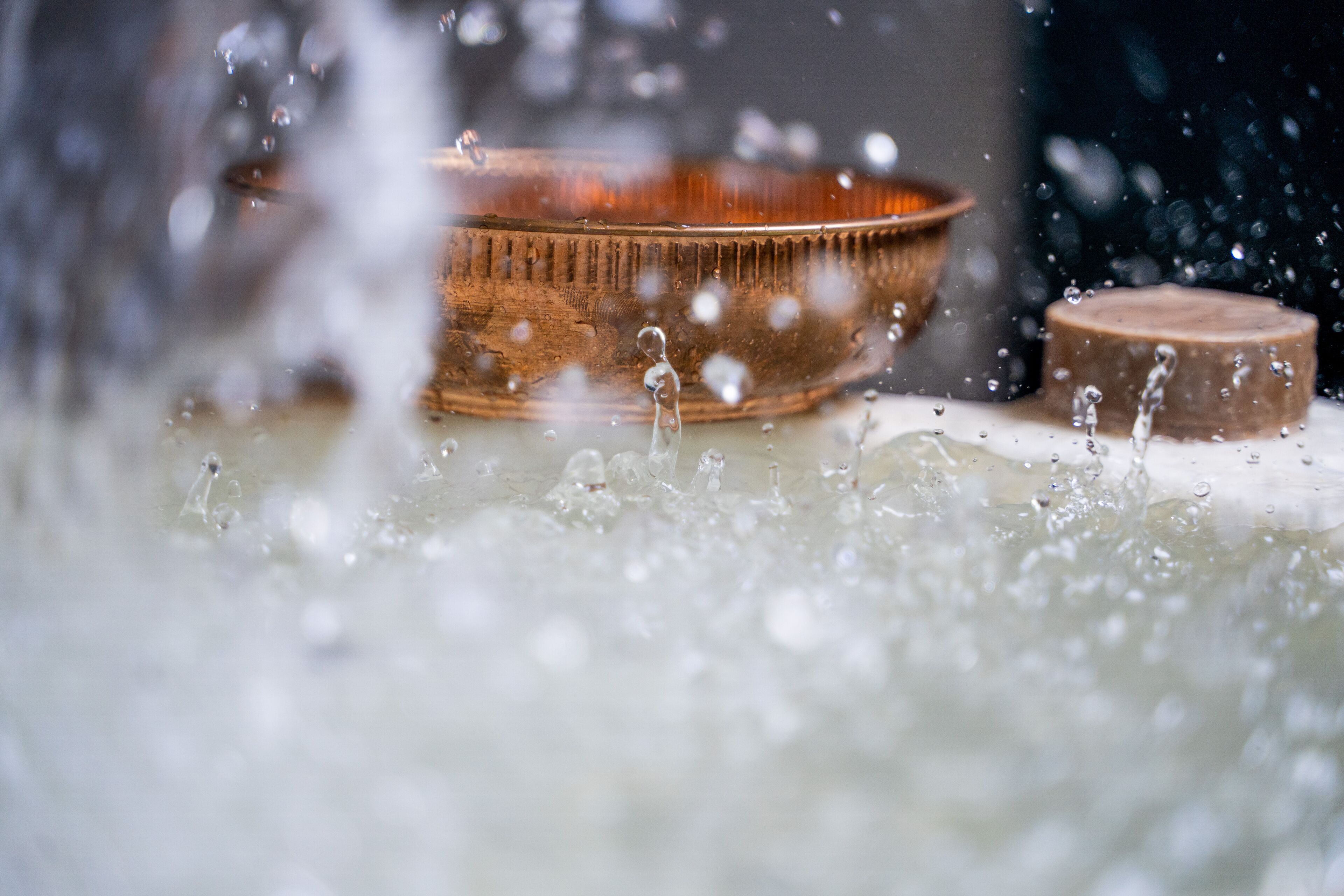 A close-up of a copper bowl with water splashing around it.