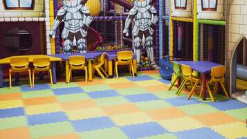 A play area with padded flooring, tables, chairs, and a climbing net.