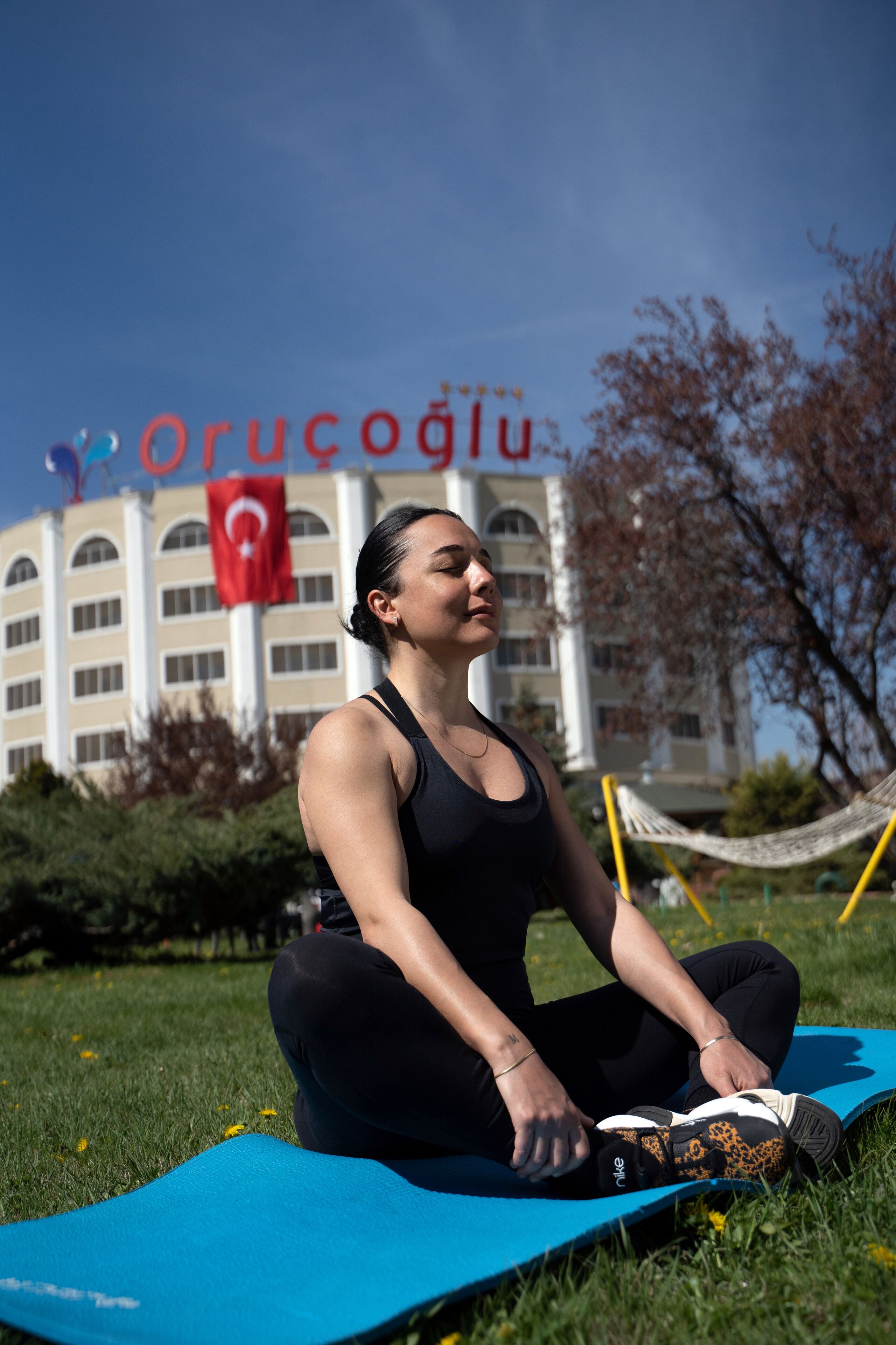A person sitting on a blue exercise mat outdoors with a building in the background.
