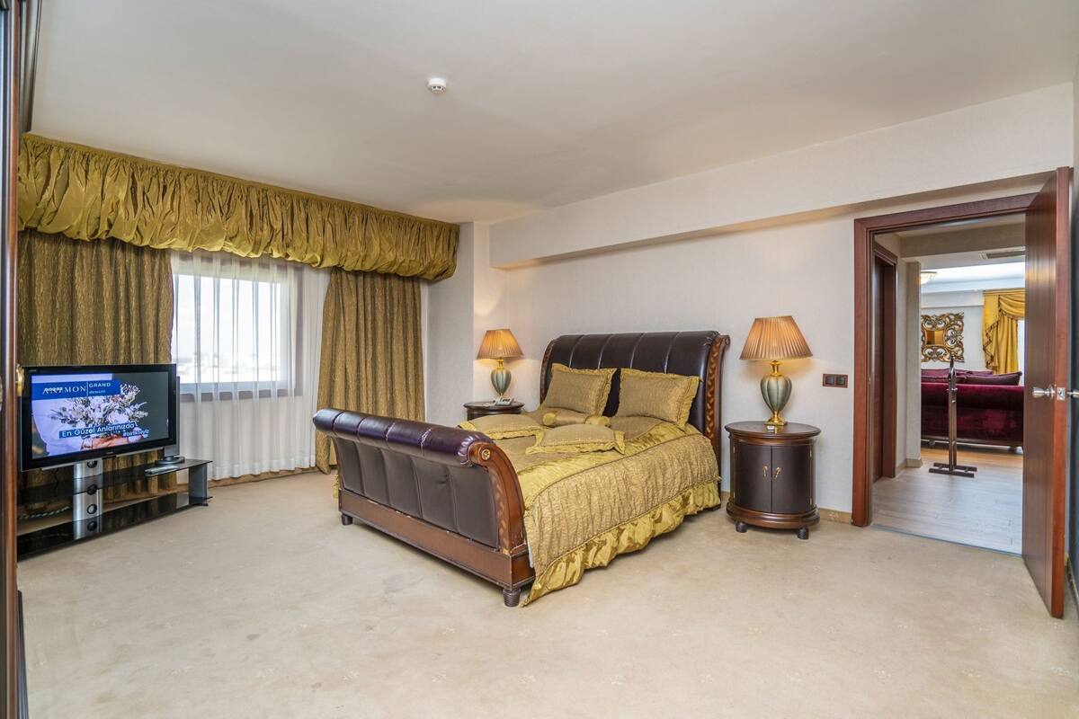 Une chambre à coucher comprenant un lit, deux tables de chevet, un téléviseur et une porte donnant sur une autre pièce.