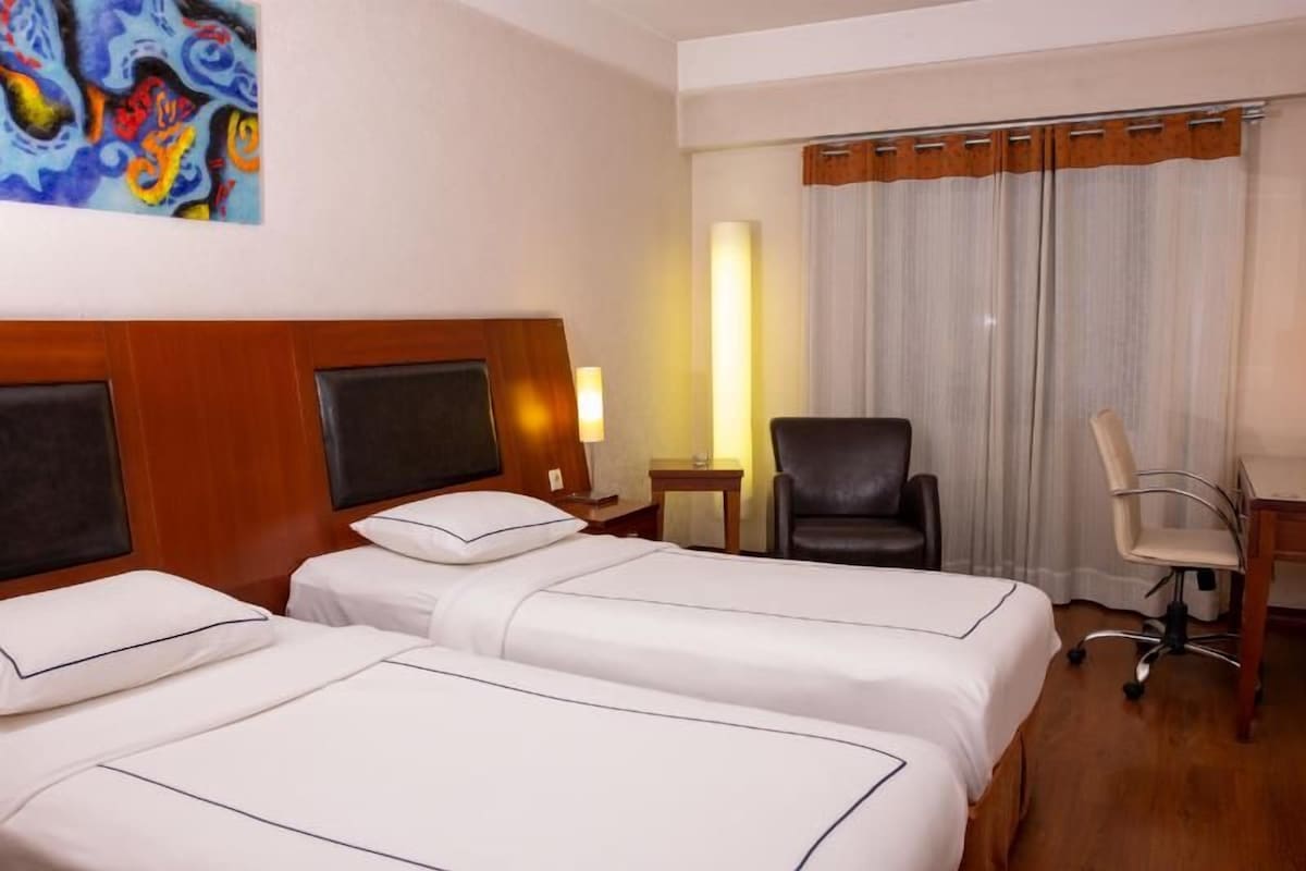 Une chambre d’hôtel avec deux lits, un bureau, une chaise et un tableau au mur.