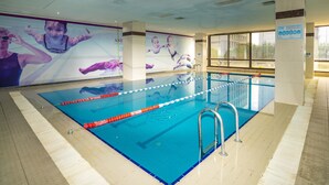 An indoor swimming pool with clear lane dividers, a lifeguard chair, and a large poster on the wall.