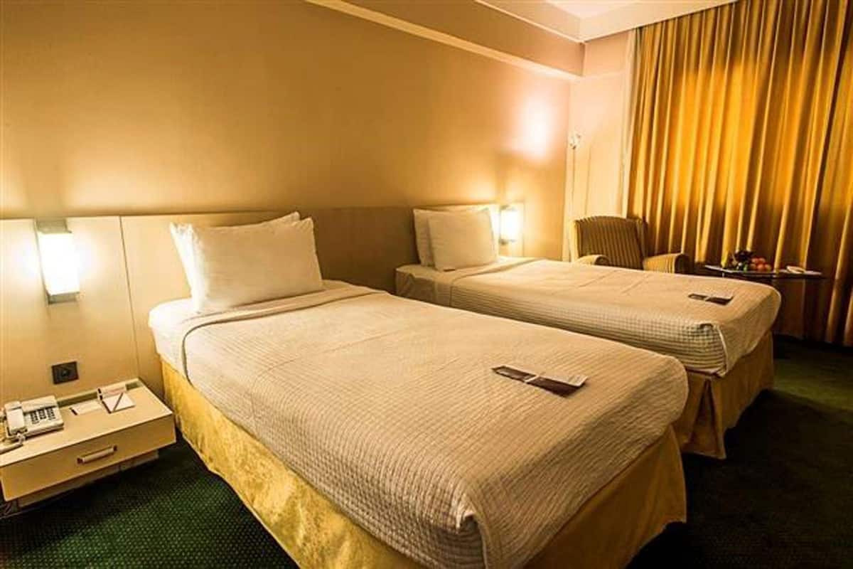 A hotel room with two beds, bedside tables, lamps, a chair, and a small table with fruits.