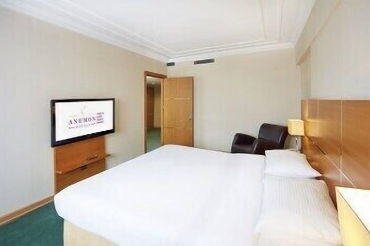 A hotel room with a bed, a TV on the wall, a desk, and a chair.