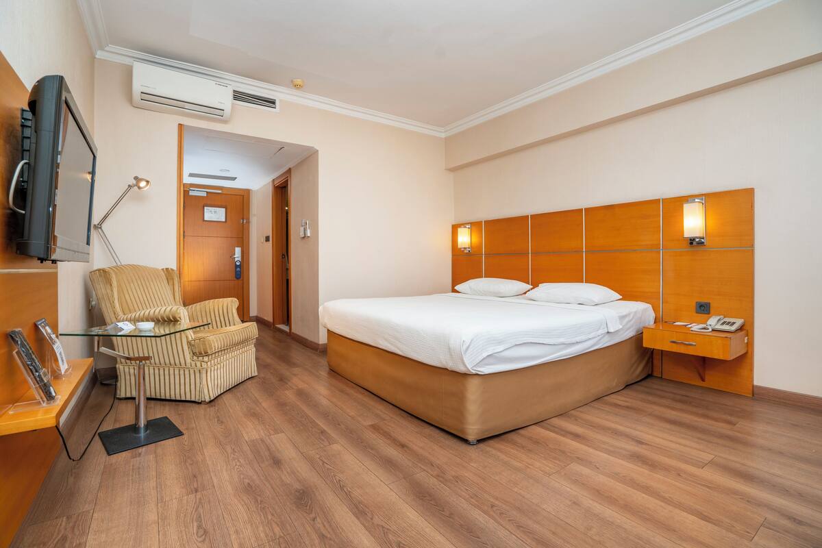 A hotel room with a bed, a chair, a desk, a TV, and a bedside table.