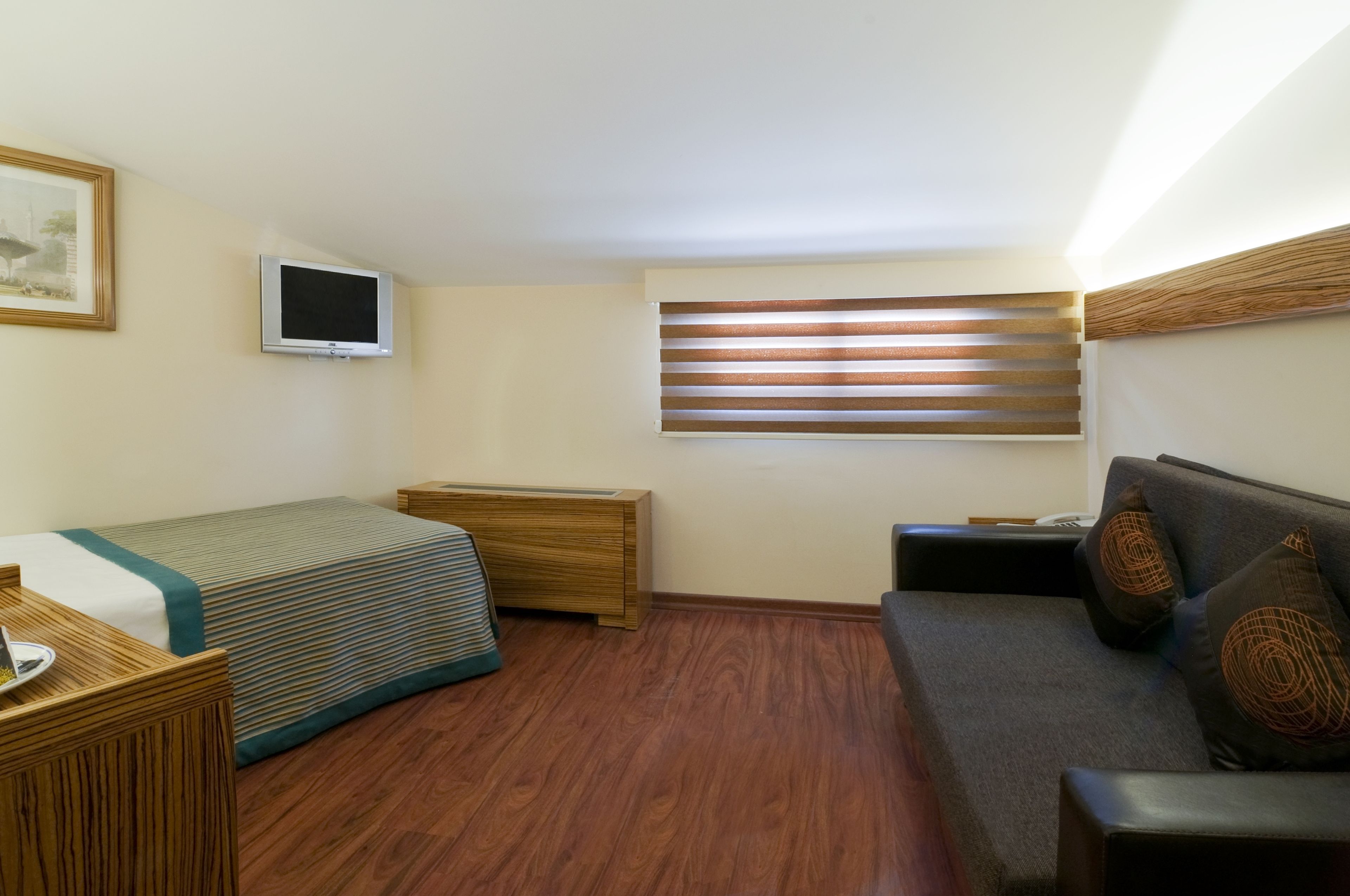 Habitación de hotel compacta con cama, sofá, televisión y ventana con persianas.