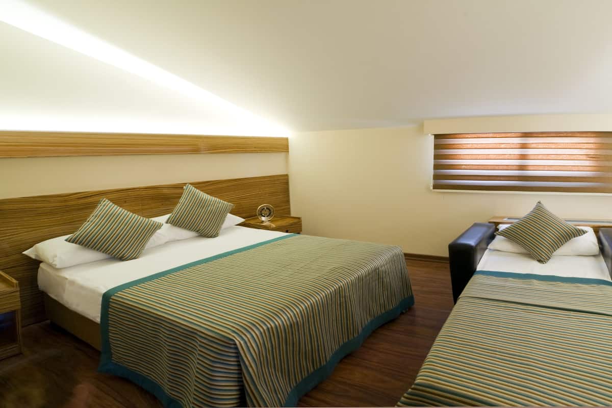 Ein Hotelzimmer mit zwei Betten, Holz-Kopfteilen, einem Nachttisch und einem Fenster mit Jalousien.