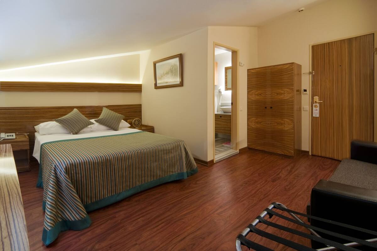Ein Hotelzimmer mit einem Bett, einem Holzschrank, einem Stuhl und einer Tür zu einem Badezimmer.