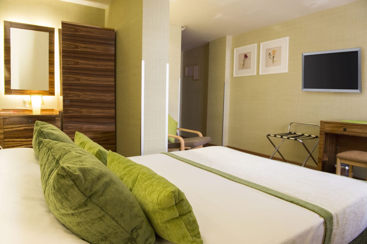 Ein Hotelzimmer mit einem Bett, einem Holzschrank, einem Schreibtisch, einem Stuhl und einem Fernseher.