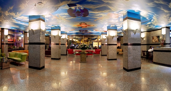 A lobby with a polished floor, a reception desk, and a ceiling with a cloud mural.