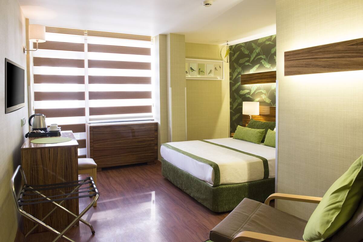 Ein Hotelzimmer mit einem Bett, einem Schreibtisch mit Lampe, einem Sessel und einem Fernseher.