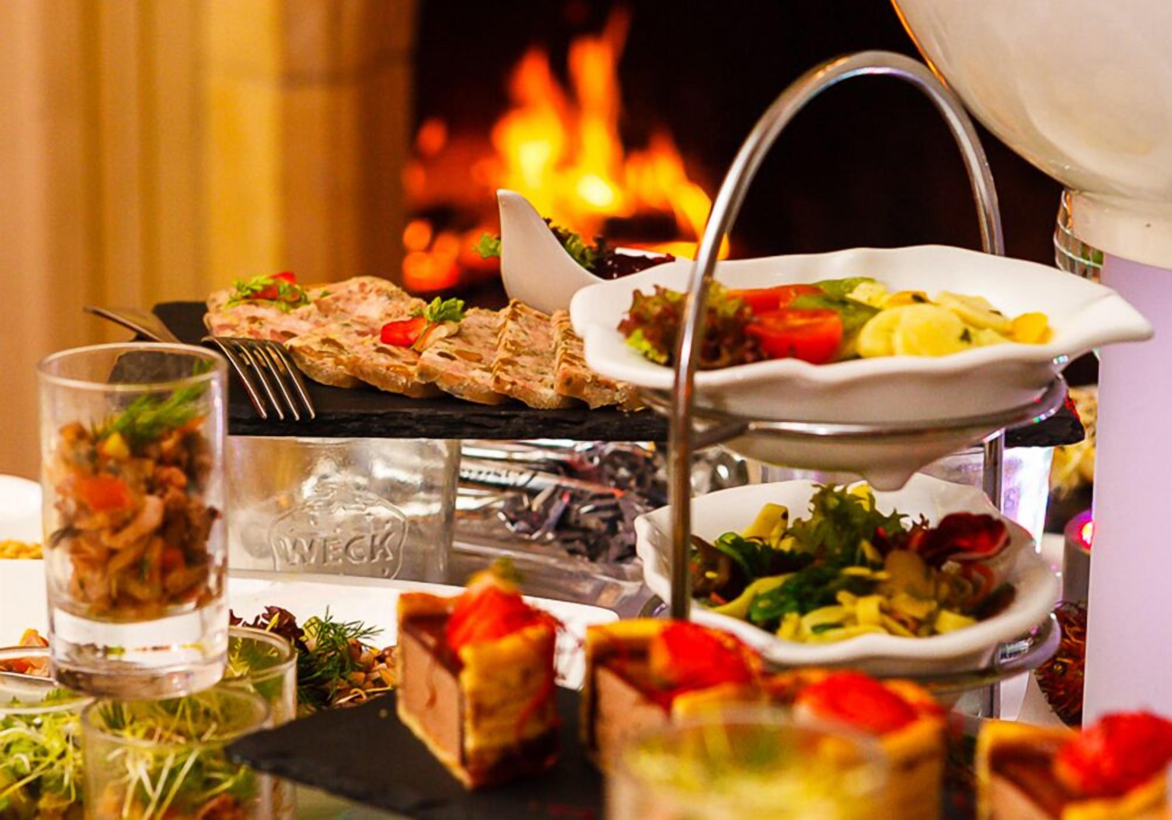 Un buffet proposant divers plats, notamment des viandes grillées et des salades, disposés sur une table devant un décor de cheminée.