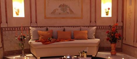 A luxurious room with a white sofa, orange cushions, a marble floor, and a large mirror.