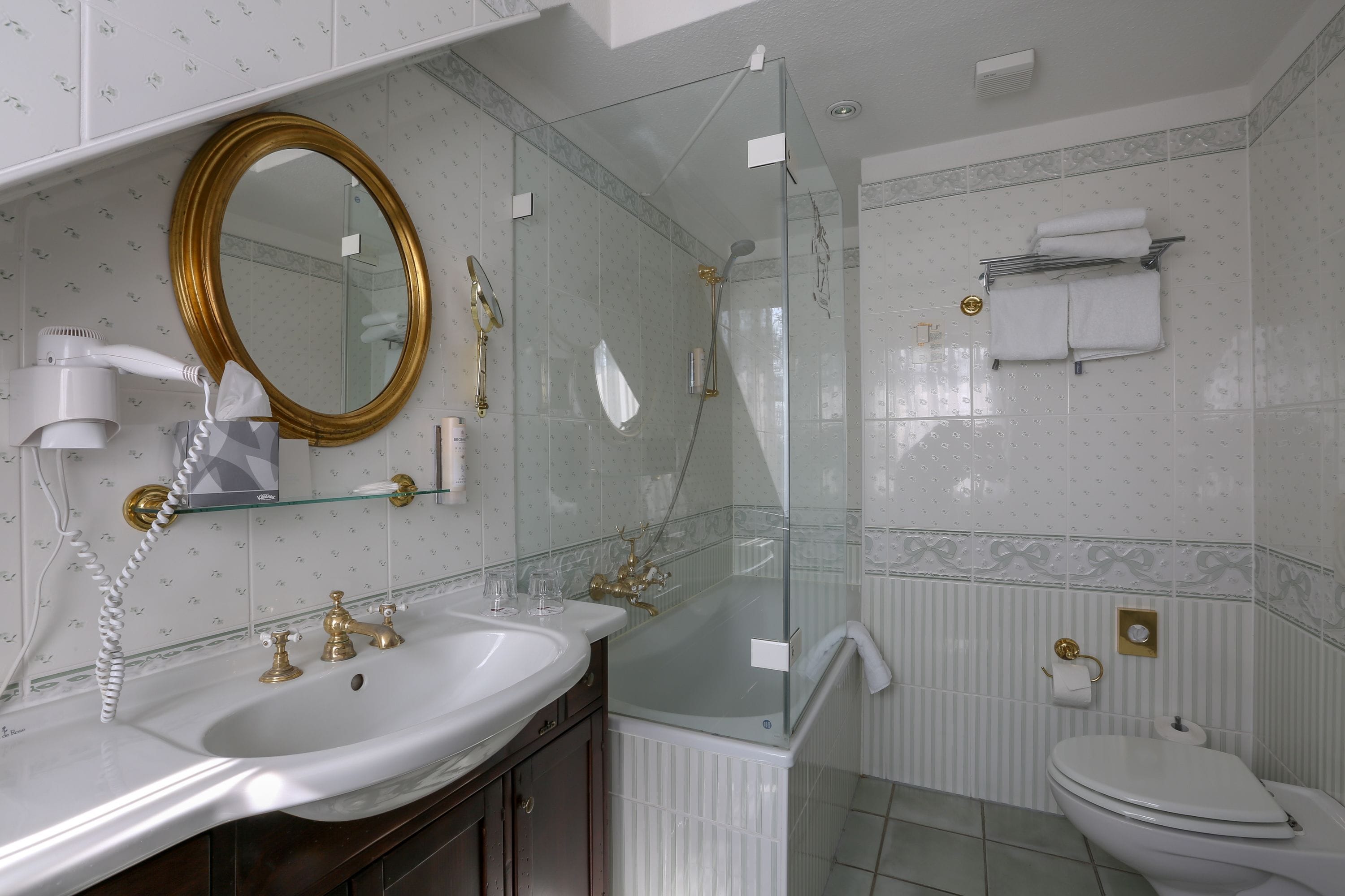 Ein Badezimmer mit einem weißen Waschbecken, goldenen Armaturen, einer Duschkabine aus Glas und einer Toilette.