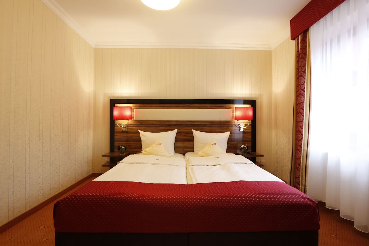 Ein Hotelzimmer mit einem großen Bett, zwei Nachttischen, einem Holz-Kopfteil und einer roten Wand als Akzent.