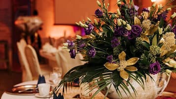 Ein Esstisch, gedeckt mit einer großen silbernen Blumenschale, einer weißen Tischdecke und Besteck.
