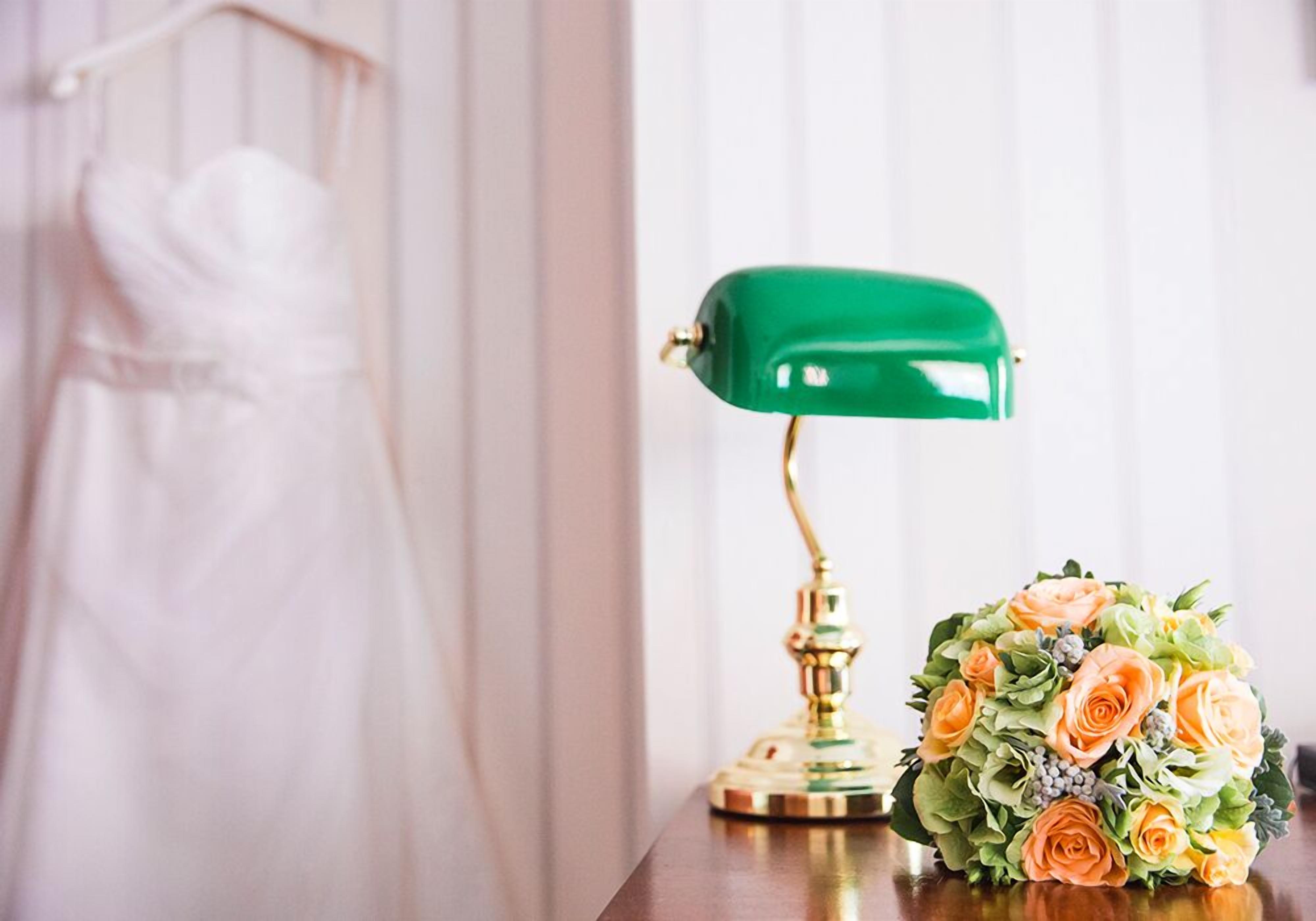 A wedding dress, a green desk lamp, and a bouquet of flowers on a table.