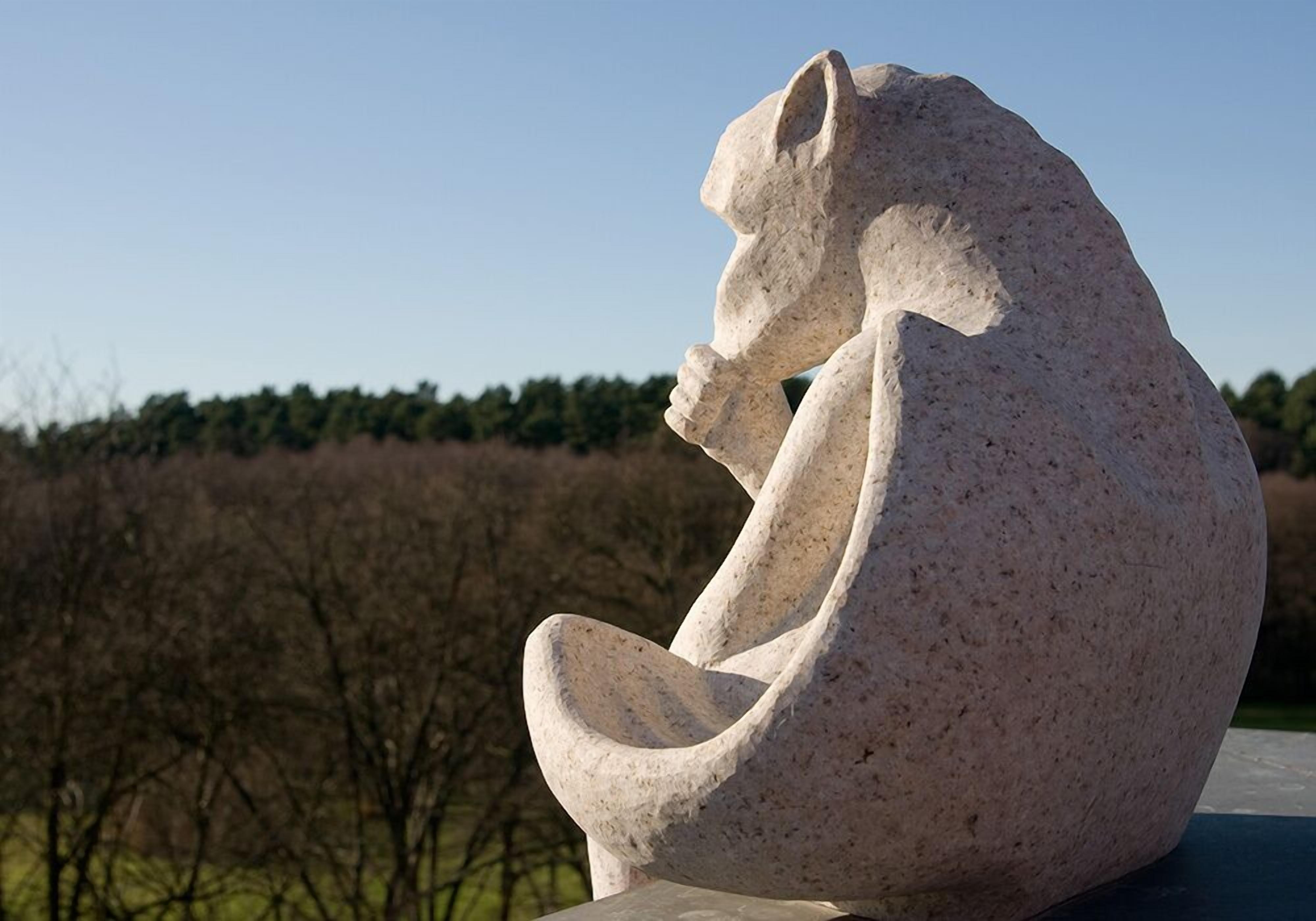 A stone sculpture of a seated figure in a park setting.