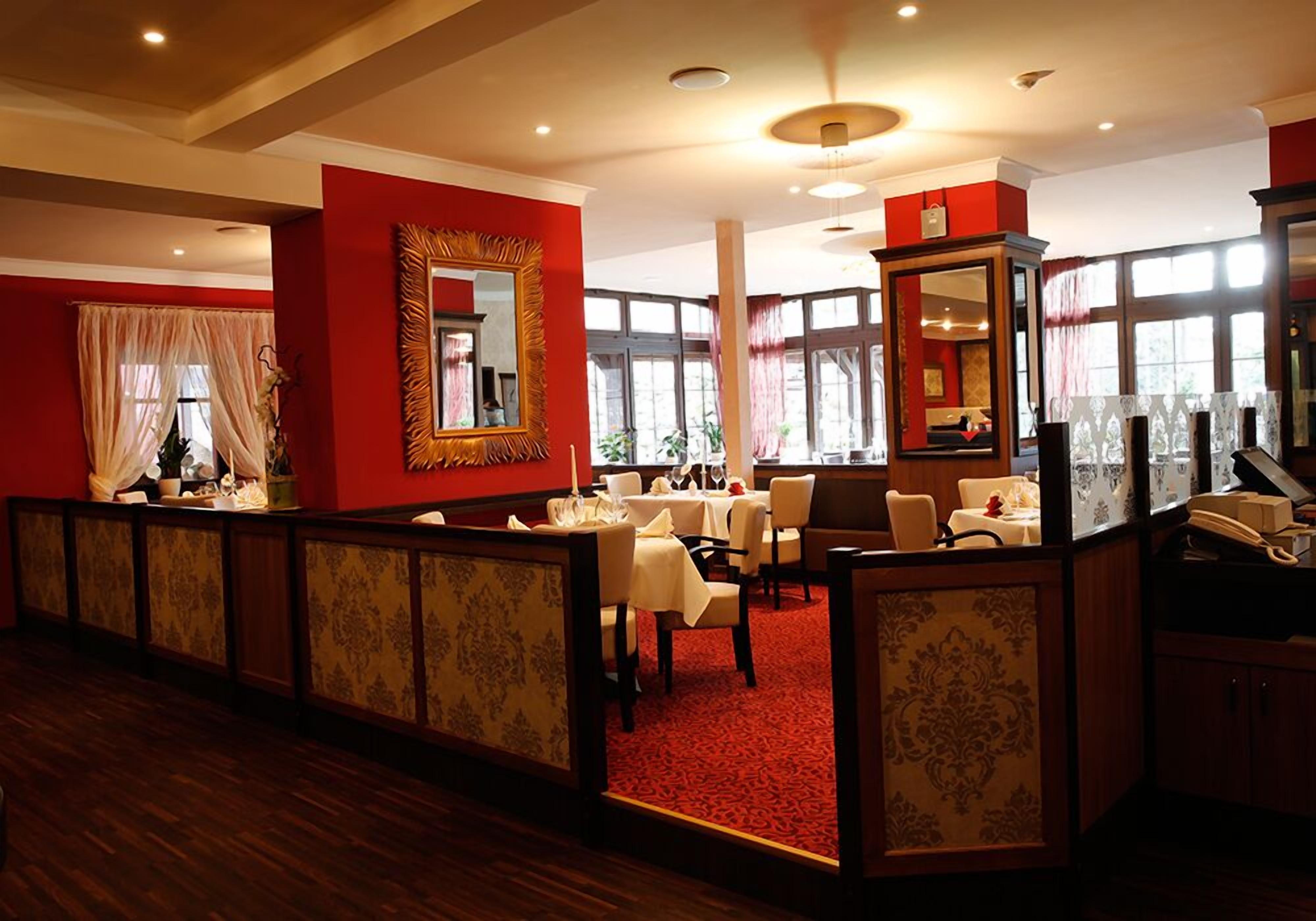 A hotel lobby with a red and beige color scheme, featuring a reception area, seating arrangements, and large windows providing natural light.