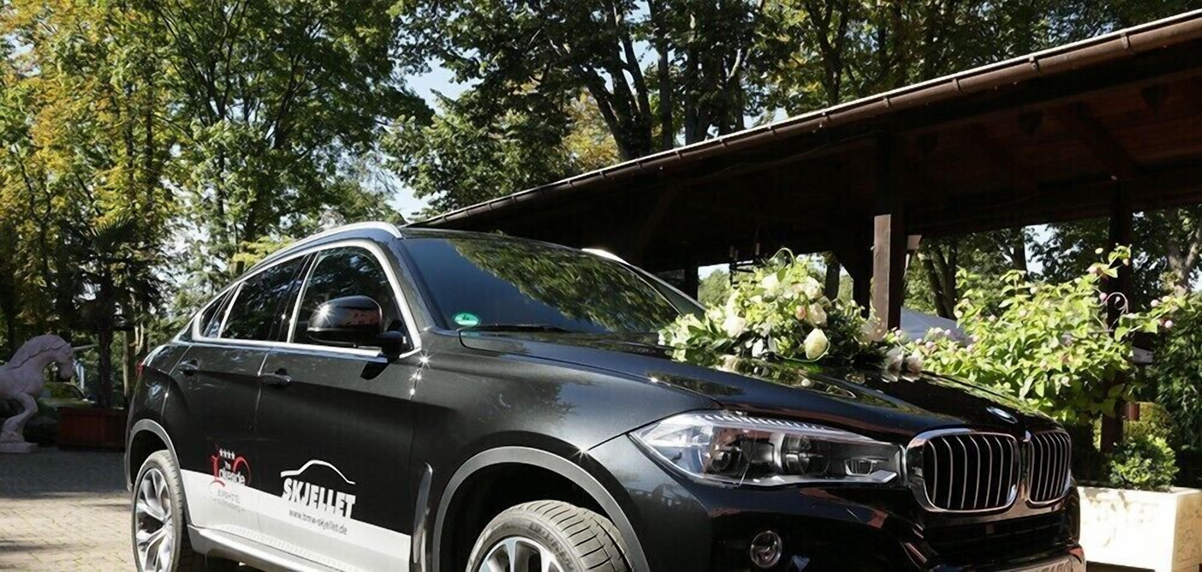 A black SUV parked in a covered outdoor area with trees and a statue in the background.