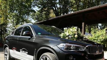 A black SUV parked in a covered outdoor area with trees and a statue in the background.