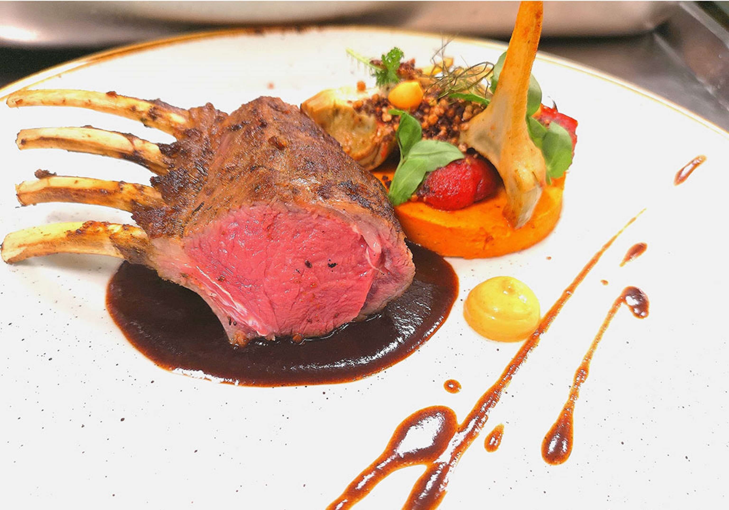 Un plato con una costilla de cordero, una porción de carne y verduras acompañantes.