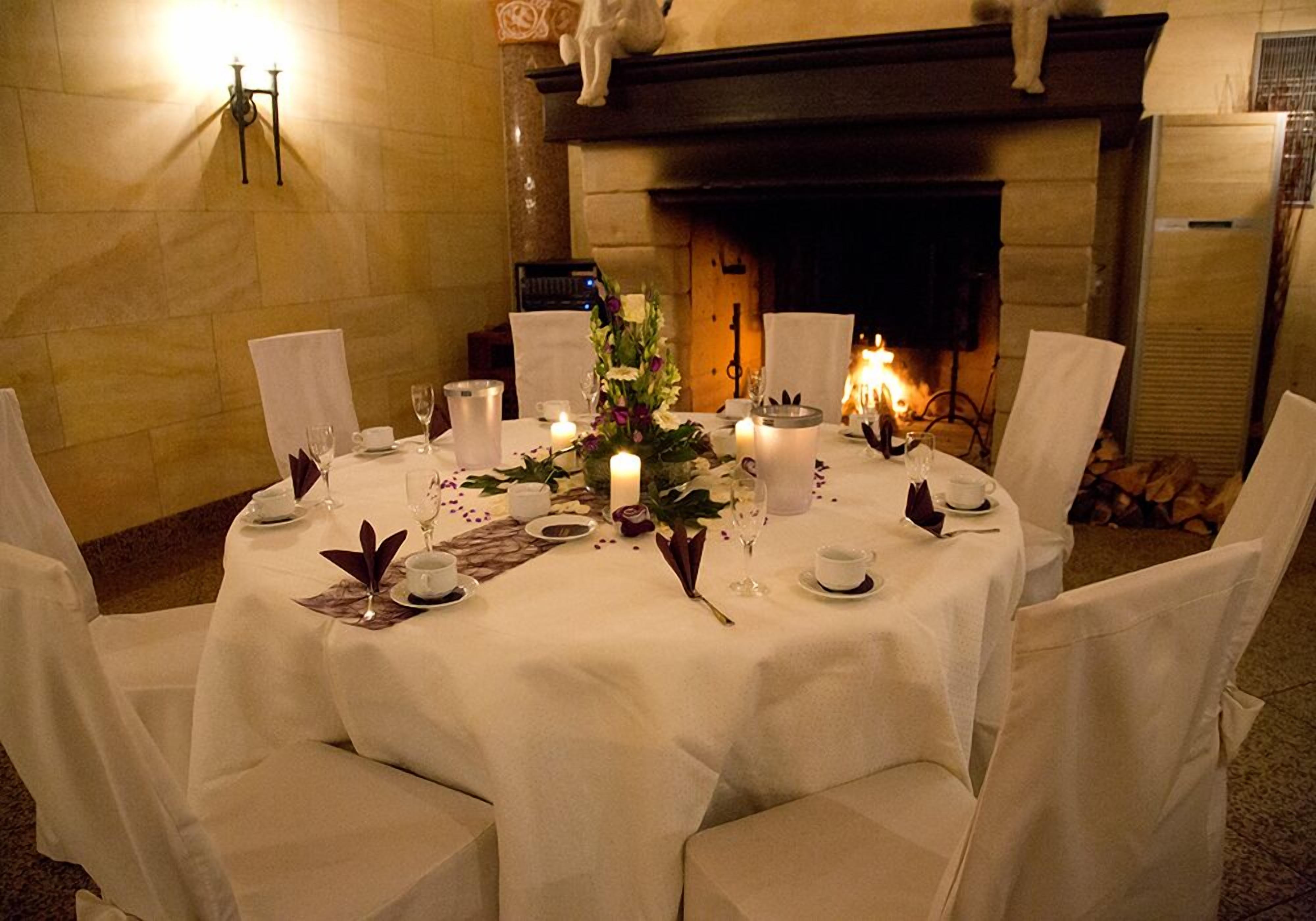 Una mesa redonda de comedor preparada para cuatro, con manteles blancos, velas y centros de mesa florales.