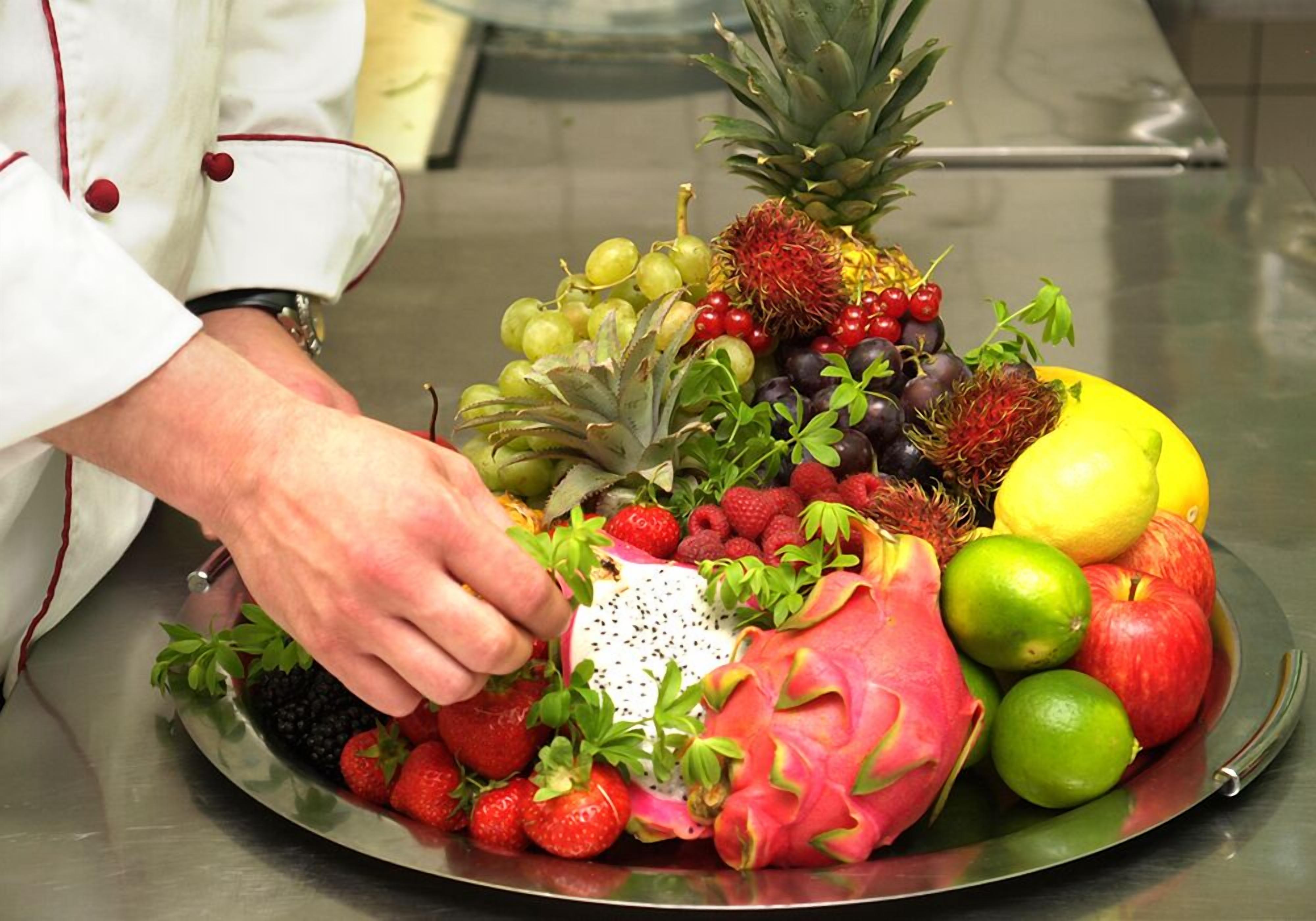 Un chef disponiendo una bandeja de frutas con diversas variedades, incluyendo fresas, uvas, pitahaya y más.