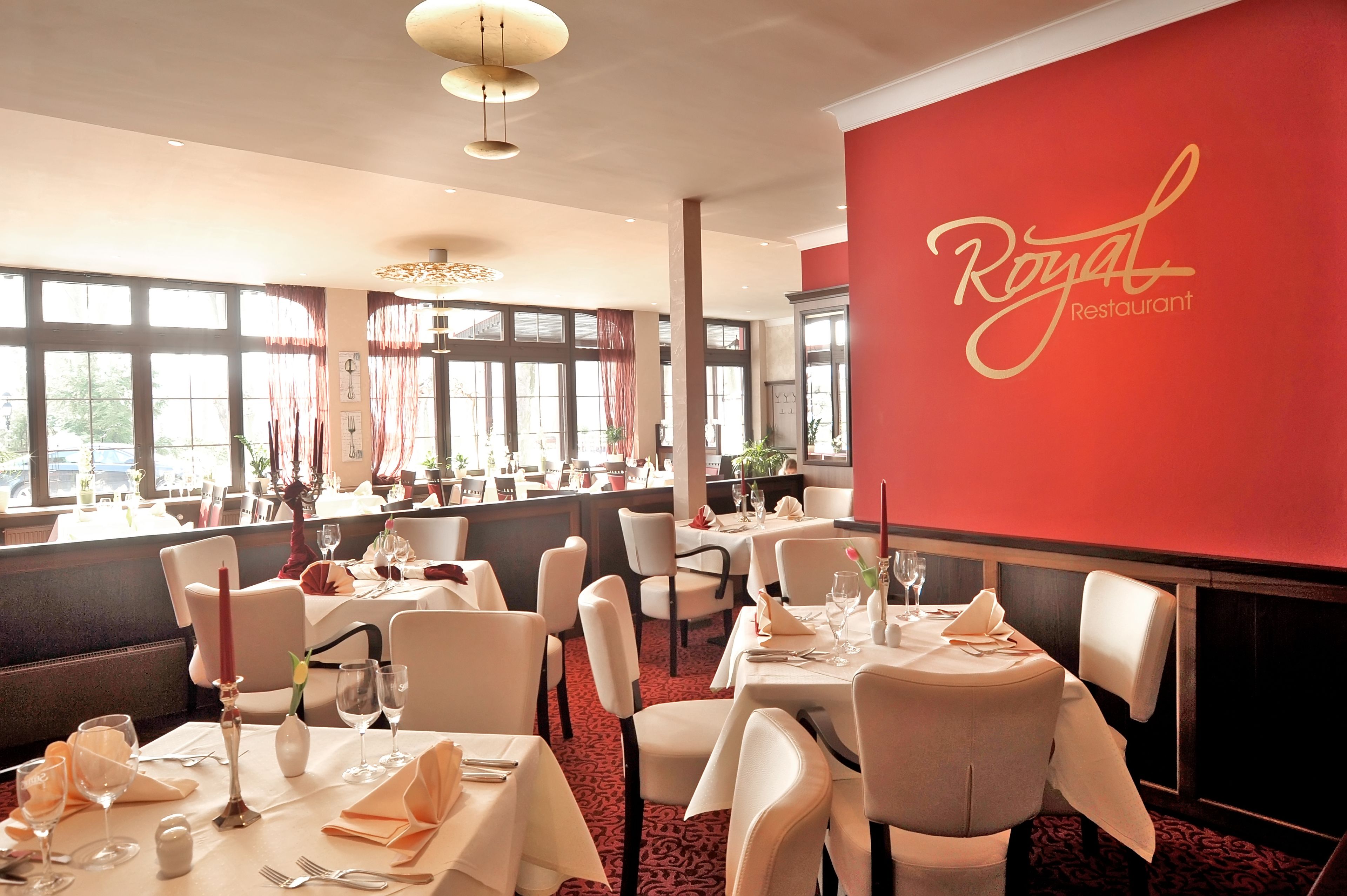 Interior de un restaurante con mesas dispuestas para comer, una pared roja con el nombre del restaurante y grandes ventanales que dejan entrar luz natural.