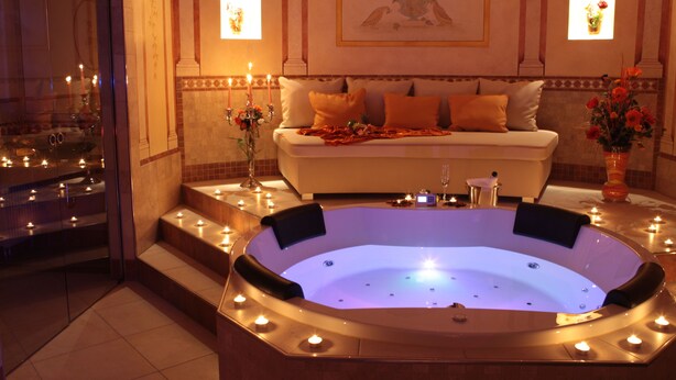 Een luxueuze badkamer met een groot bad, een witte bank en kaarsen.
