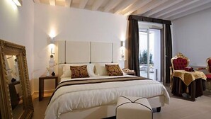 A hotel room with a large bed, a sitting area with a chair, a table, and a mirror. - Al Canal Regio (Venice)