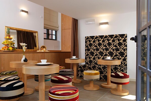 A modern interior with round wooden tables, colorful striped ottomans, a mirror, and a patterned wall. - Al Canal Regio (Venice)
